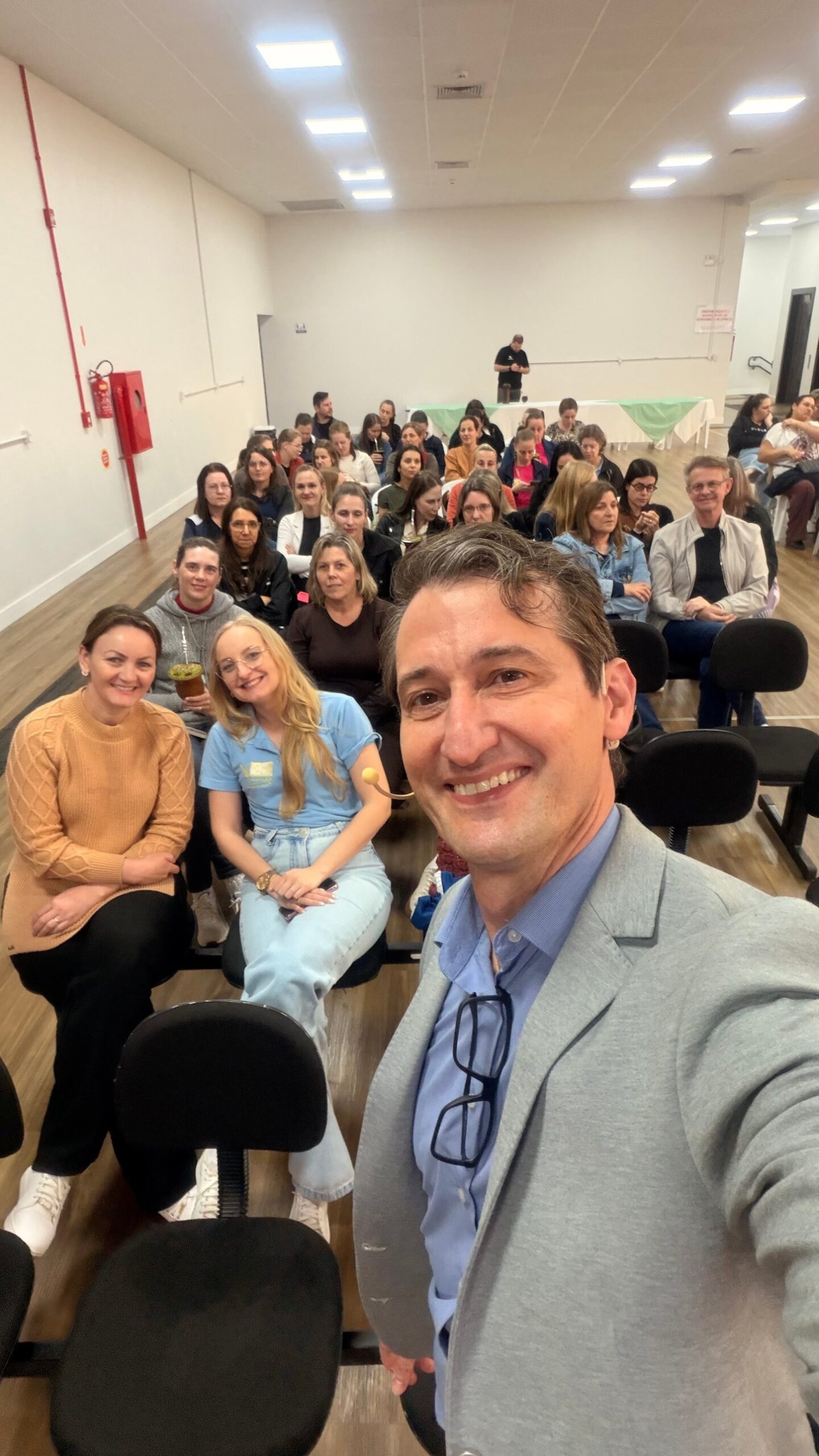 Edney Prigol sorri em selfie à frente de um grande grupo de servidores da educação de Iporã do Oeste reunidos no auditório